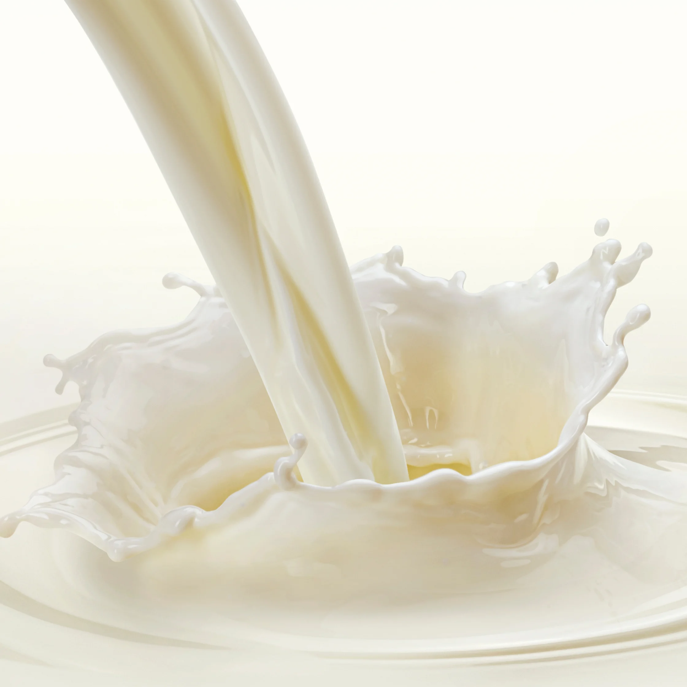 A thick stream of creamy milk pours into a pool, creating a dramatic crown-shaped splash with droplets against a bright, clean background.