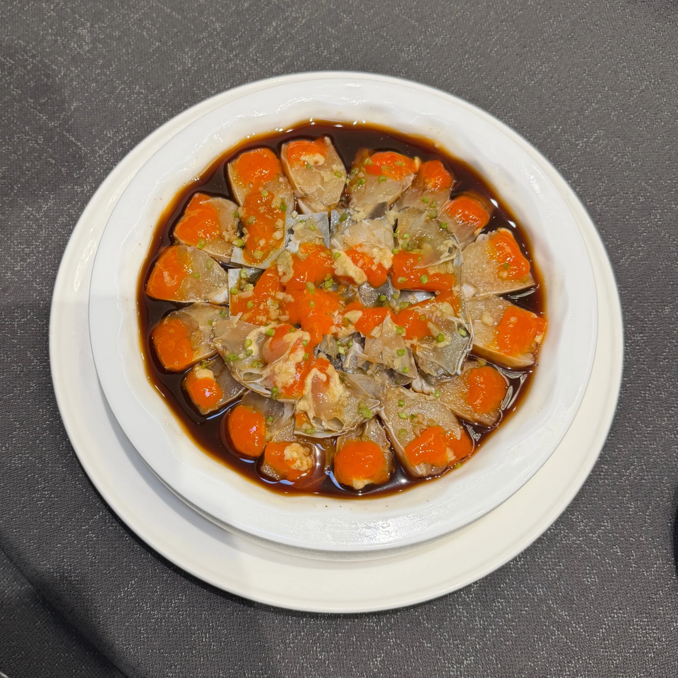Overhead view of a white bowl filled with braised meat and bright orange carrot chunks in dark gravy, sprinkled with herbs on a gray tablecloth.